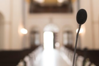 A podium mic with pews blurred in the background, representing a pastor preparing to start a sermon