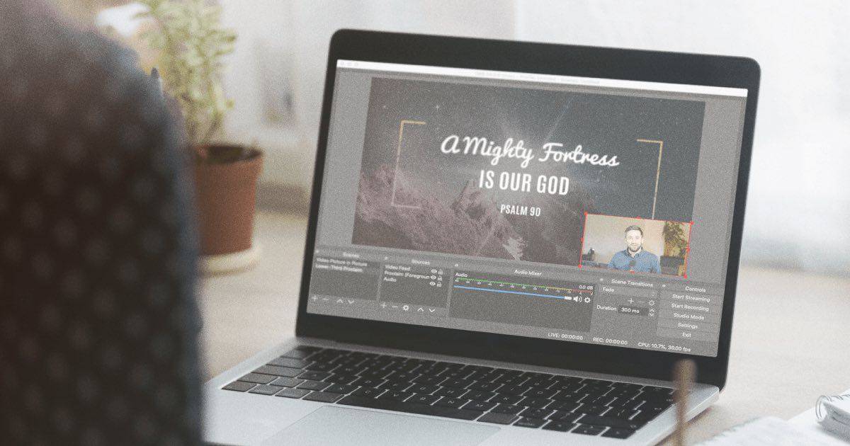 person at a table watching a church live stream on a laptop