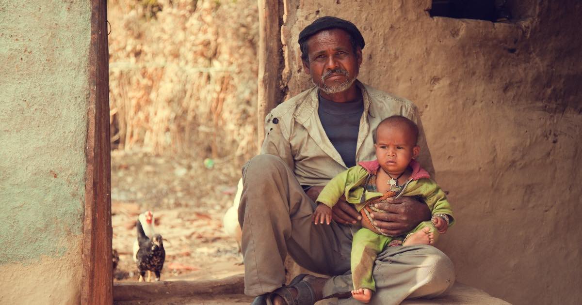 poor villager man and baby sit on the ground