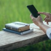 person outside does Bible study with an app and physical Bible