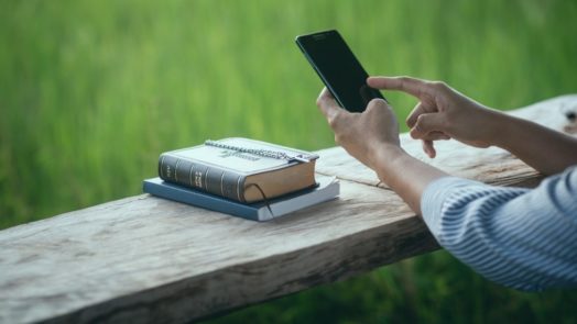 person outside does Bible study with an app and physical Bible