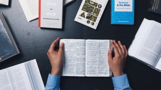 Seminary Student Reading the Bible Surrounded by Other Books and Commentaries