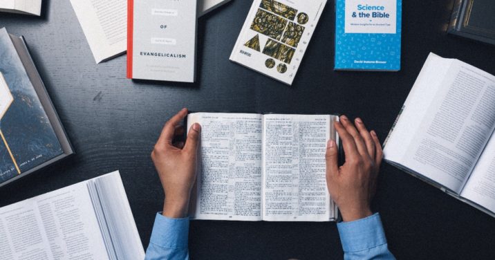 Seminary Student Reading the Bible Surrounded by Other Books and Commentaries