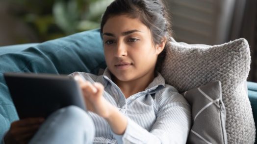 woman on couch reading devotional Bible commentary on tablet