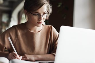 young woman at desk studies the Bible with laptop and open notebook