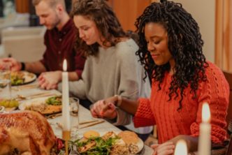 friends at table hold hands to pray for their meal after reading Thanksgiving Bible verses